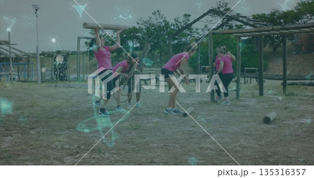 Moving group of six women lifting logs and handling ropes on grassy field, with tire obstacles 135316357