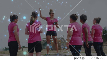 Leading fitness instructor on platform directing trainees on dusty field with tablet timer whistle 135316366