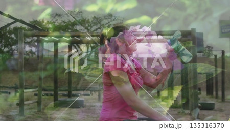 Woman in pink shirt drinking from green water bottle at obstacle course, with frames, beams, tires 135316370