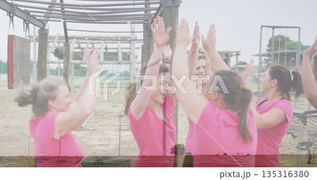 High-fiving six women wearing pink shirts at obstacle course, with monkey bars and rope nets 135316380