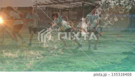 Pulling children gripping braided rope on grassy playground field under sun, with wooden play bars 135316408