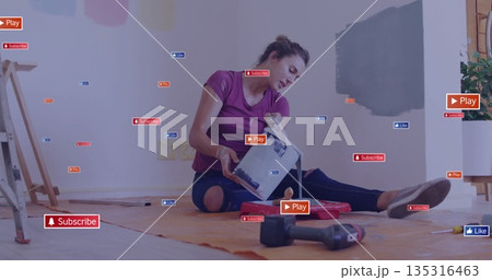 Woman in purple t-shirt pouring grey paint into red roller tray inside home, with paint swatches 135316463