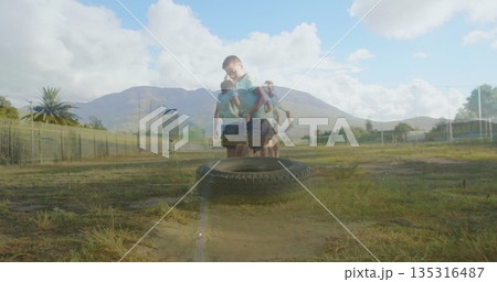 Pulling tire by chain, boy wearing light blue polo and navy shorts exercising on school field Pulling tire by chain, boy wearing light blue polo and navy shorts exercising on school field 135316487