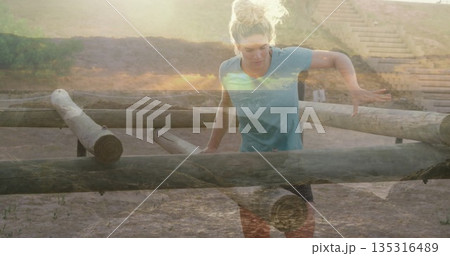 Negotiating light-skinned woman jumping low wooden logs barrier on sandy course, with wooden steps Negotiating light-skinned woman jumping low wooden logs barrier on sandy course, with wooden steps 135316489