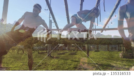 Training fitness partners navigating wooden obstacle course in grassy field, with hanging ropes 135316533