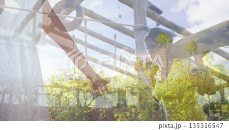 Gripping woman in sleeveless top raising arms under pergola beams, with ropes and yellow flowers Gripping woman in sleeveless top raising arms under pergola beams, with ropes and yellow flowers 135316547