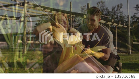 Performing sit-ups woman wearing workout clothes on grass beneath wooden bars, trainer guiding Performing sit-ups woman wearing workout clothes on grass beneath wooden bars, trainer guiding 135316569