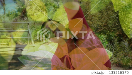 Stretching woman in pink jacket lifting arms overhead in park, with stone surface, wooden bench 135316570