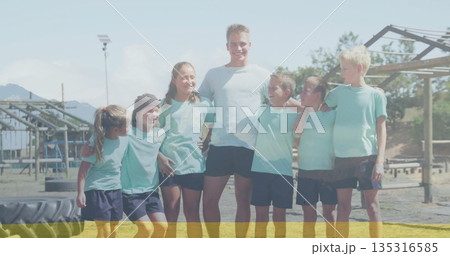 Standing together coach and children wearing teal sportswear at obstacle course, with tractor tire Standing together coach and children wearing teal sportswear at obstacle course, with tractor tire 135316585