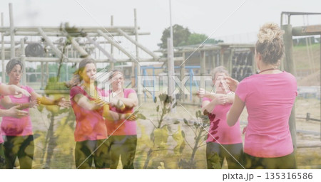 Stretching women in matching pink tops and black leggings following leader at obstacle course beams 135316586