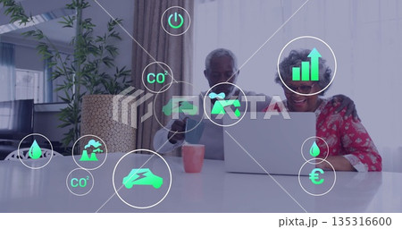 Analyzing senior African American couple using silver laptop in living room, with green icons 135316600