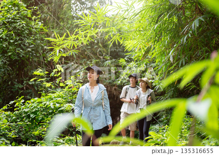 Woman tourist walking in front of man and friend while holding cane during forest hiking or trekking Woman tourist walking in front of man and friend while holding cane during forest hiking or trekking 135316655
