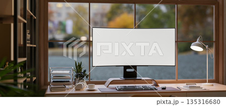 White screen computer and coffee with headphone on wooden table in glass wall living room or office. 135316680