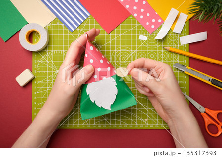 Making a craft. Hands glue the nose to the gnome's body. Creative process. Making a craft. Hands glue the nose to the gnome's body. Creative process. 135317393