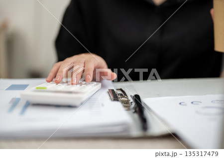 Close up of businesswoman or office worker's hand using a calculator over documents at working table 135317479