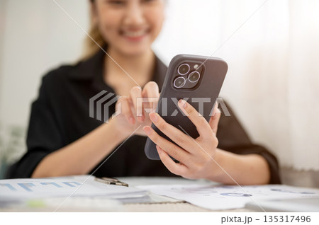 Close up of asian businesswoman or office worker smiling while looking at phone over working table. 135317496