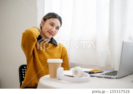 Asian woman student or office worker touching or massaging pained neck in front of a laptop on table 135317528