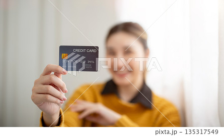 Blurred face young asian woman extending one hand showing a blue credit card to camera. Bank ad. 135317549