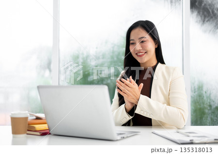 Smart asian businesswoman or office worker in suit clapping hands in front of laptop at working table. Smart asian businesswoman or office worker in suit clapping hands in front of laptop at working table. 135318013