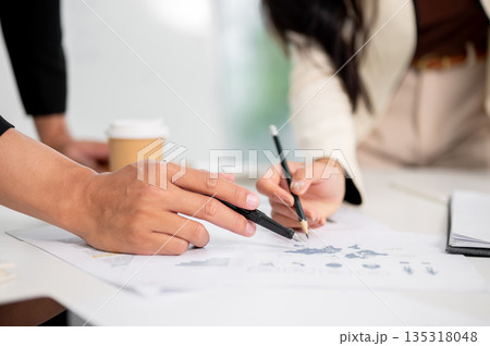 Close up businesswoman and man's hand holding pencil pointing on document at working table in office Close up businesswoman and man's hand holding pencil pointing on document at working table in office 135318048