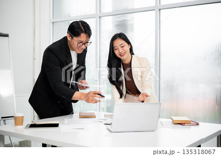 Smiling businesswoman and man or office worker looking at laptop together over table with document. Smiling businesswoman and man or office worker looking at laptop together over table with document. 135318067