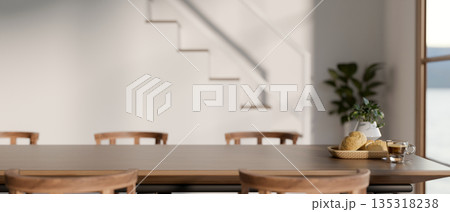 Breads and coffee on wooden dining table and chairs beside stairs in modern house or office building Breads and coffee on wooden dining table and chairs beside stairs in modern house or office building 135318238