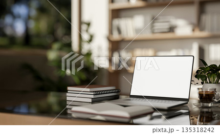 White screen laptop with books and coffee cup on glass top wooden table in a sunlit living room. White screen laptop with books and coffee cup on glass top wooden table in a sunlit living room. 135318242