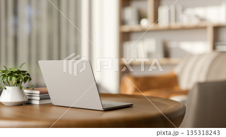 Laptop and books with pot plant on round wooden table and armchair aside bookshelf in living room. Laptop and books with pot plant on round wooden table and armchair aside bookshelf in living room. 135318243