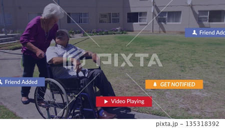 Pushing senior woman propelling wheelchair along paved path, showing digital banners, windows 135318392