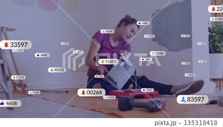 Pouring woman in purple shirt, leggings tilting paint can into tray at home, with floating icons 135318418