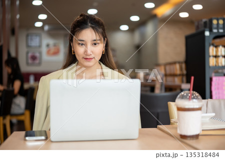 Asian woman looking and using the laptop doing assignment or watching video in a cafe or coffee shop Asian woman looking and using the laptop doing assignment or watching video in a cafe or coffee shop 135318484