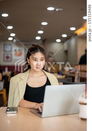 Asian woman looking and using a laptop doing assignment or watching video in a cafe or coffee shop. Asian woman looking and using a laptop doing assignment or watching video in a cafe or coffee shop. 135318486
