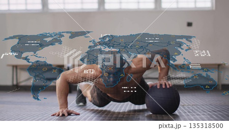 Man wearing shorts doing single-arm push-up using medicine ball on mat in gym, with digital overlay 135318500