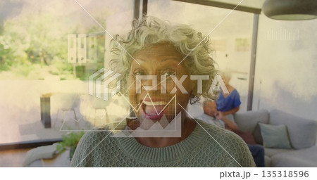 Smiling senior woman wearing gray sweater sitting on sofa in living room, with floating data charts Smiling senior woman wearing gray sweater sitting on sofa in living room, with floating data charts 135318596
