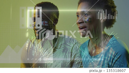 Watching woman and man reacting in living room, with face-painted national flags and chart overlays 135318607