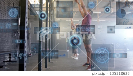 Extending arms overhead man wearing maroon shirt at training gym, with digital HUD overlay Extending arms overhead man wearing maroon shirt at training gym, with digital HUD overlay 135318623