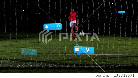 Kicking soccer player wearing red uniform on grass pitch at night, with net, ball, digital icons Kicking soccer player wearing red uniform on grass pitch at night, with net, ball, digital icons 135318671