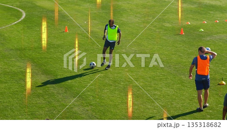 Dribbling yellow bib athlete controlling soccer ball on grass pitch, with orange and green cones Dribbling yellow bib athlete controlling soccer ball on grass pitch, with orange and green cones 135318682