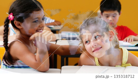 Smiling two girls leaning together and conversing in school classroom, with notebooks and pencils 135318712