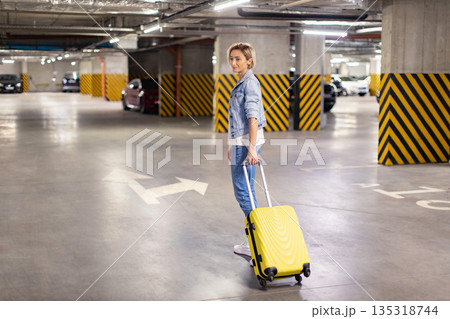 A woman with a yellow suitcase stands in a parking garage, ready to travel 135318744