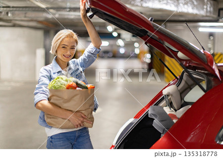 A smiling woman loads groceries into the trunk of her car in an underground parking garage A smiling woman loads groceries into the trunk of her car in an underground parking garage 135318778