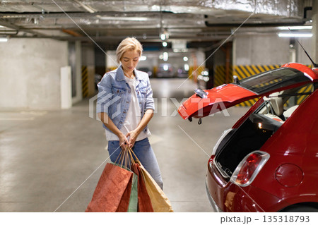 A woman loads shopping bags into the trunk of her car in a parking garage 135318793