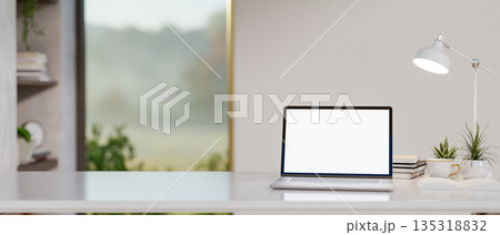 White screen laptop with coffee or tea cup under lamp light on shiny table in a glass door room. 135318832