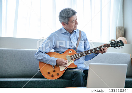 ノートパソコンでギターのオンラインレッスンを受けるシニア男性 135318844