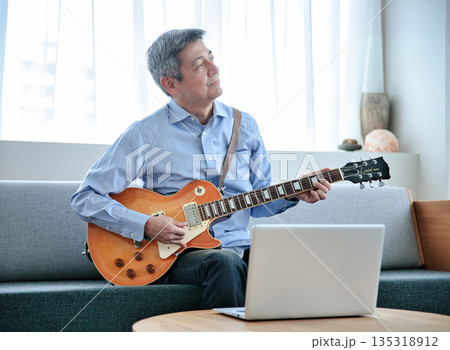 ノートパソコンでギターのオンラインレッスンを受けるシニア男性 135318912