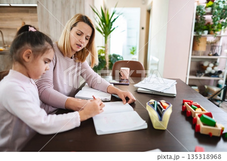 Engaging mother and daughter studying together in a cozy home setting Engaging mother and daughter studying together in a cozy home setting 135318968