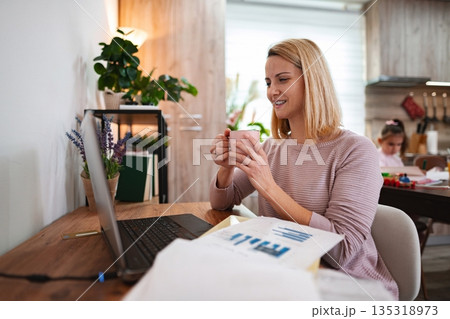 Engaging in a virtual meeting while enjoying a warm drink at home Engaging in a virtual meeting while enjoying a warm drink at home 135318973