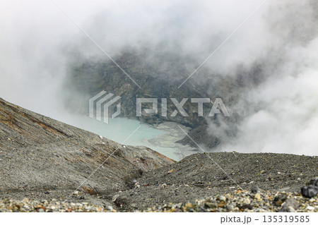 View of the crater opening of erupting volcano. Crater with volcanic gas fumaroles. Clouds and steam in the sky. View of the crater opening of erupting volcano. Crater with volcanic gas fumaroles. Clouds and steam in the sky. 135319585