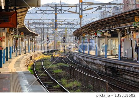 Empty railway station platform with double-track railroad railway or train tracks in suburb train station, perspective view. Travel and transportation concept. Empty railway station platform with double-track railroad railway or train tracks in suburb train station, perspective view. Travel and transportation concept. 135319602