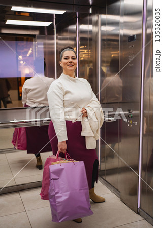 Joyful shopper with vibrant bags in a modern elevator setting Joyful shopper with vibrant bags in a modern elevator setting 135320035